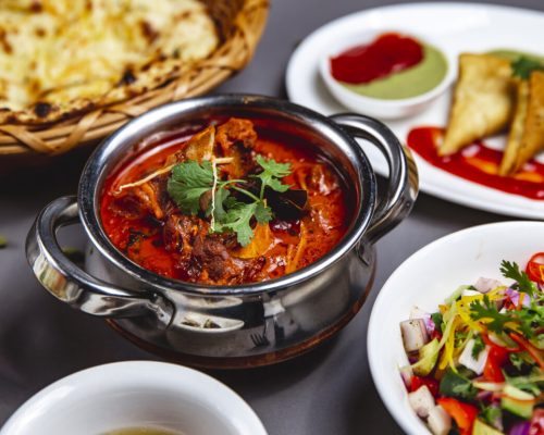 side lamb ragout with fried onion carrot tomato sauce greens and vegetable salad on the table